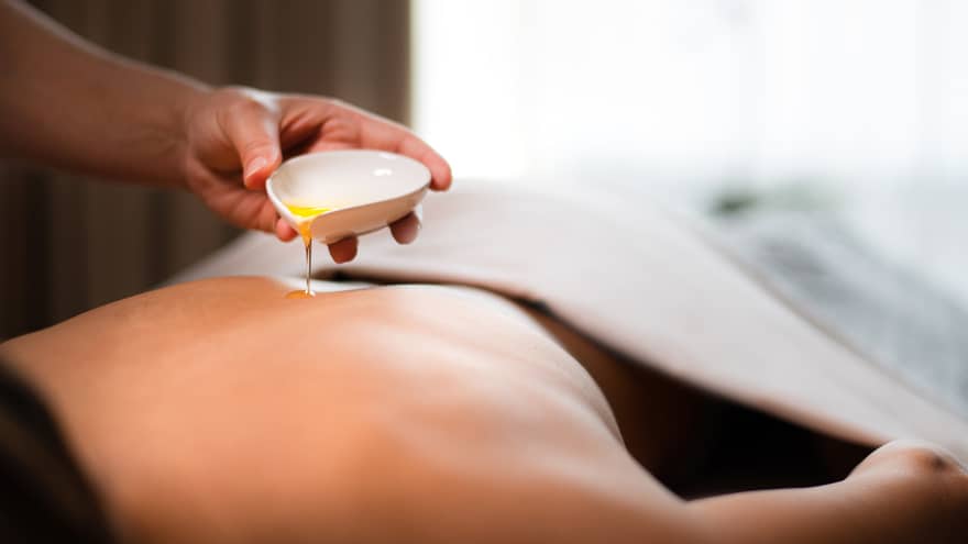 A spa staff member pouring liquid onto a woman?s back.