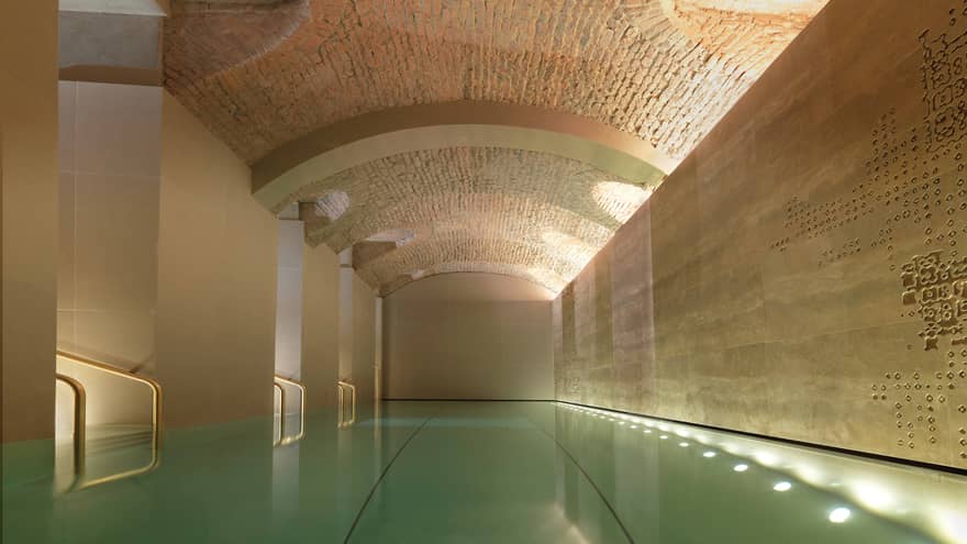 Indoor lap swimming pool with gold railings under curved stone ceiling
