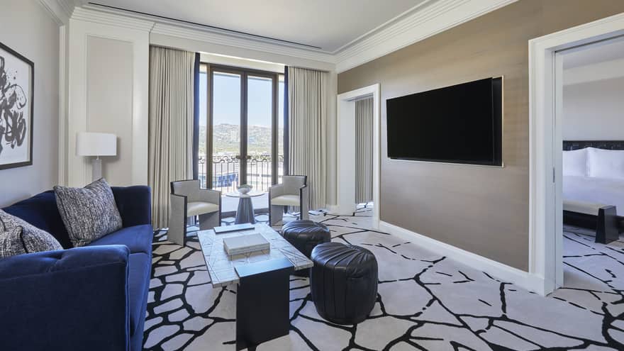 Living room with royal blue sofa, black and white carpet, wall-mountain TV, and an entrance into bedroom