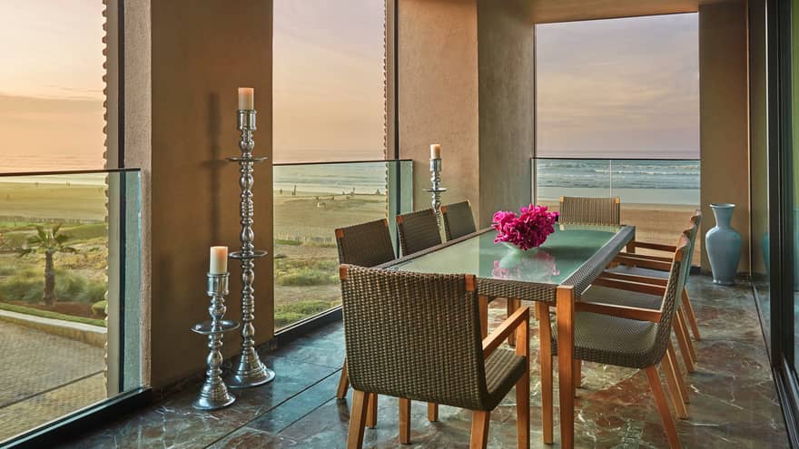 Balcony dining table with wicker chairs, fresh pink flowers, tall silver pillar candles, ocean views