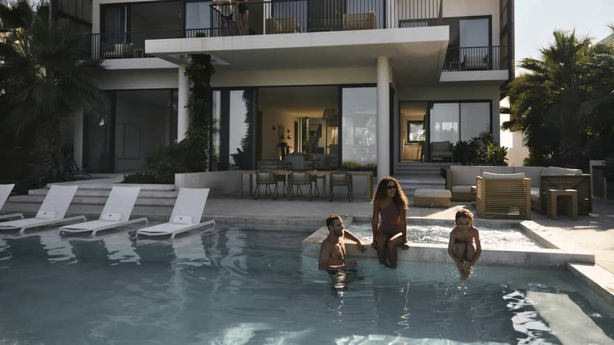A woman, man and young child sit on edge of private pool at luxury residence in tropical setting