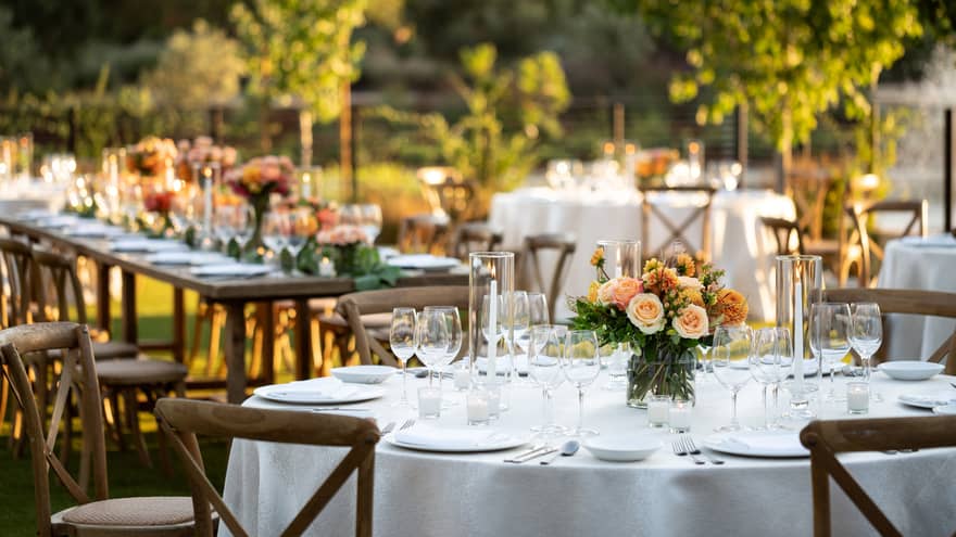 Elegant outdoor wedding reception tables adorned with white linens and peach floral centerpieces in a vineyard.