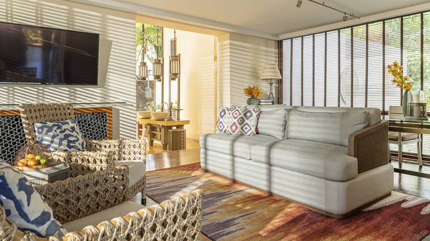 The sun streams into a living room through wooden window shutters