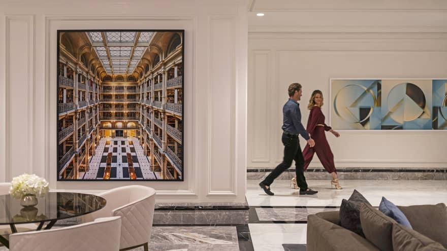 A couple walking through the hotel lobby, there is art on the wall behind them.