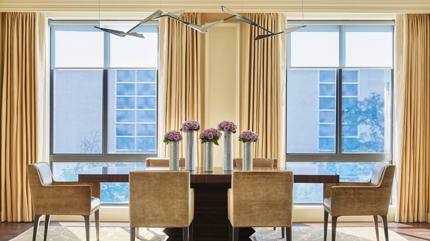 Imperial Suite modern dining table with golden brown velvet dining chairs around long wood table with tall silver vases, purple flowers