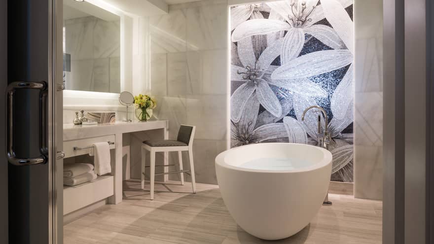 Grand Suite master bathroom white free-standing tub under mosaic tile wall with floral pattern, vanity