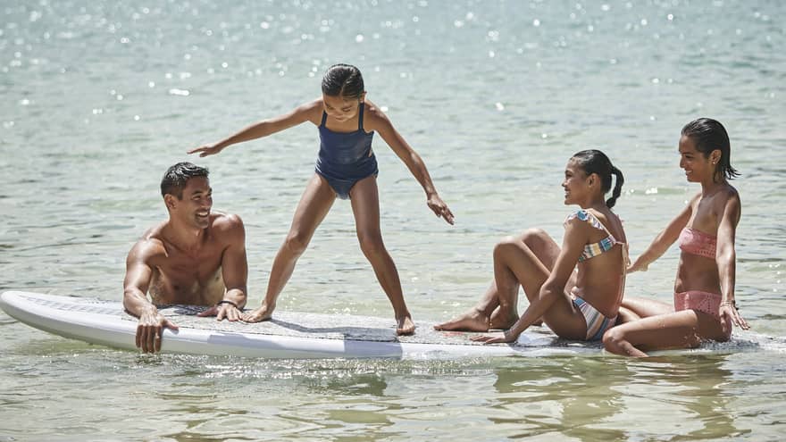A family sitting on a large surf or paddleboard.