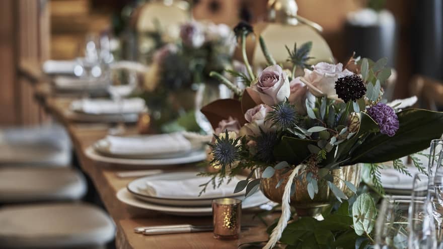 Close-up view of a beautifully arranged wedding table at Four Seasons Whistler, showcasing an elegant and rustic floral centerpiece with soft pink roses, purple flowers, and lush greenery. The table is set with pristine white plates, silver cutlery, and crystal glassware, all laid out on a natural wood table that adds a touch of warmth to the sophisticated decor.,Close-up view of a beautifully arranged wedding table at Four Seasons Whistler, showcasing an elegant and rustic floral centerpiece with soft pink roses, purple flowers, and lush greenery. The table is set with pristine white plates, silver cutlery, and crystal glassware, all laid out on a natural wood table that adds a touch of warmth to the sophisticated decor.