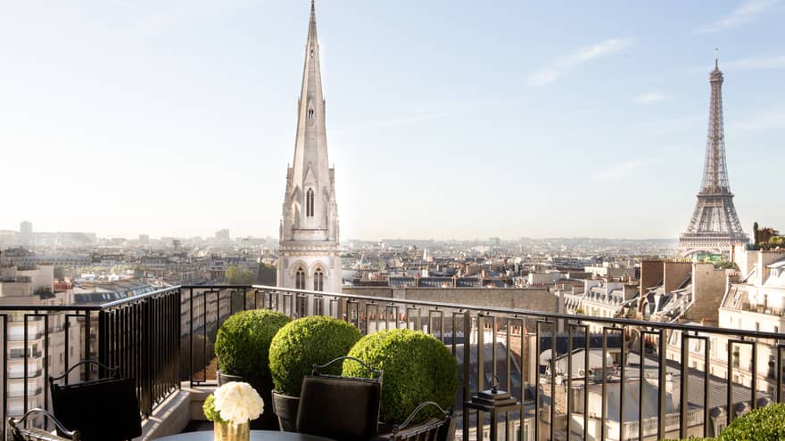 Patio dining table with white roses, potted shrubs iron balcony overlooking Paris rooftops, cathedrals