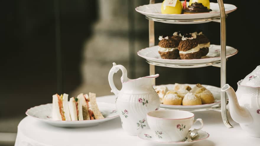 Floral teapot and teacup with sandwiches and desserts.