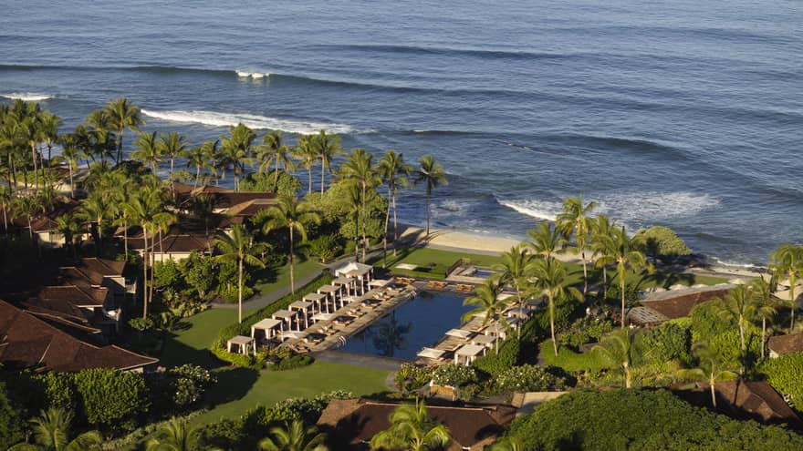 Tropical resort pool lined with cabanas and palm trees, next to the beach and ocean