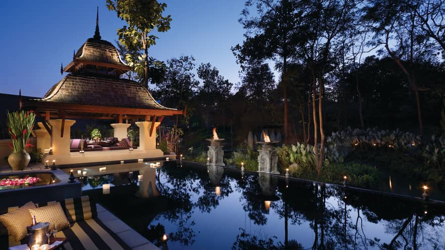 Candles. torches glow around private resort villa swimming pool, patio, sofas under wood gazebo