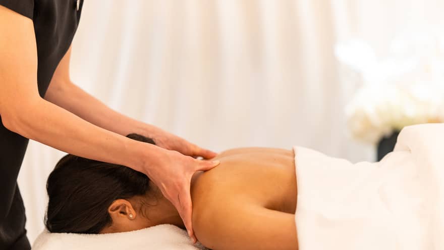 Spa therapist massaging shoulders of guest lying facedown on white spa table