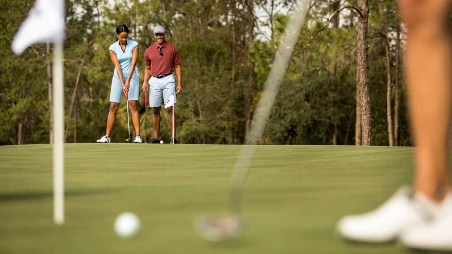 View past golfer to smiling couple preparing to putt on golf course