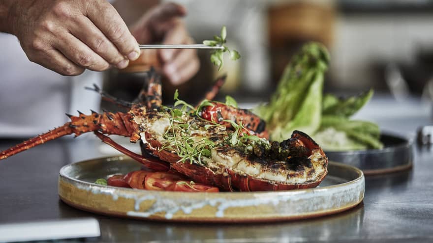 Close-up of chef garnishing grilled half lobster with herbs
