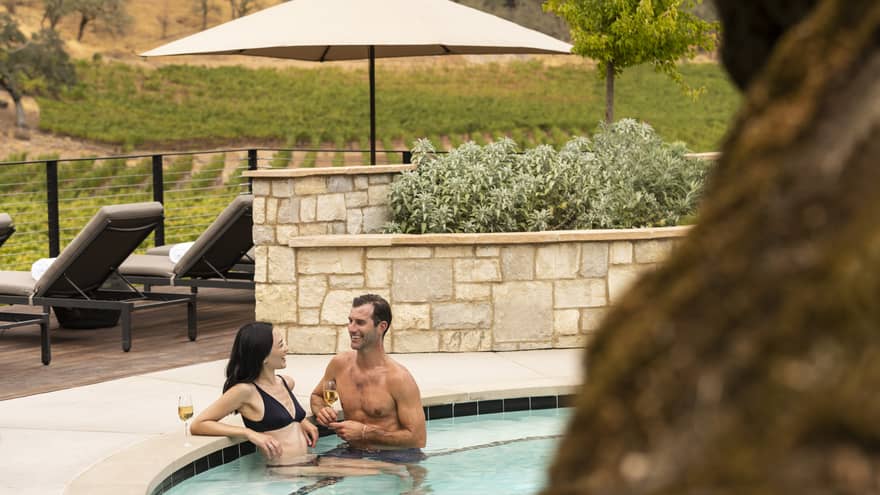 Man and woman sitting in pool holding wine glasses.