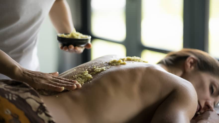 Spa staff rubs thick salt rub down woman's bare spine
