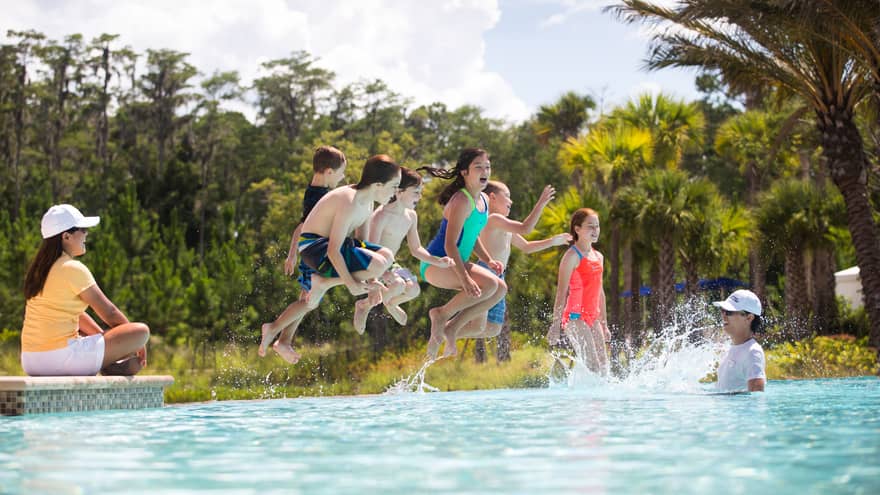 Group of children wearing swimsuits jump into outdoor swimming pool