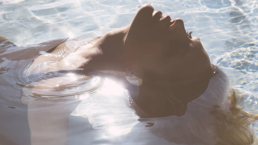 Close-up of woman's head as she floats on her back in pool, sunlight reflecting, her hair flowing in water 
