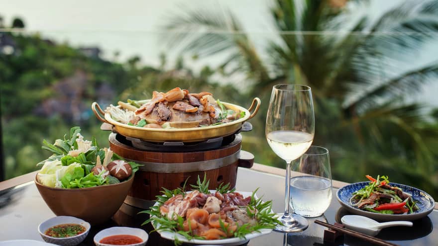 Four plates of food, glass of water and white wine, tropical scenery in background