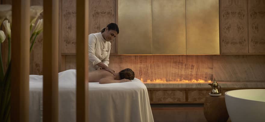 Person facedown on white spa table receiving massage from spa therapist