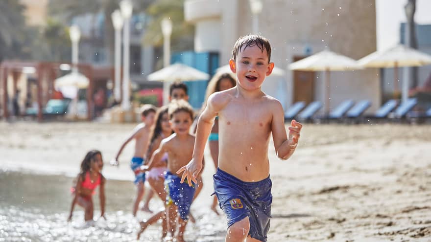Young children in swimsuits run in a row on sandy beach