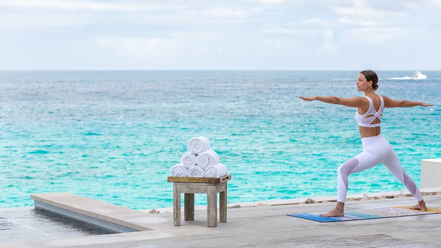 A woman doing yoga with the ocean behind her.