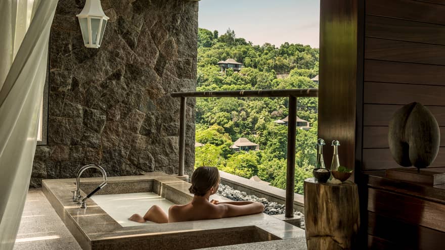 Back of woman sitting in rectangular hot tub, looking out open wall at mountain