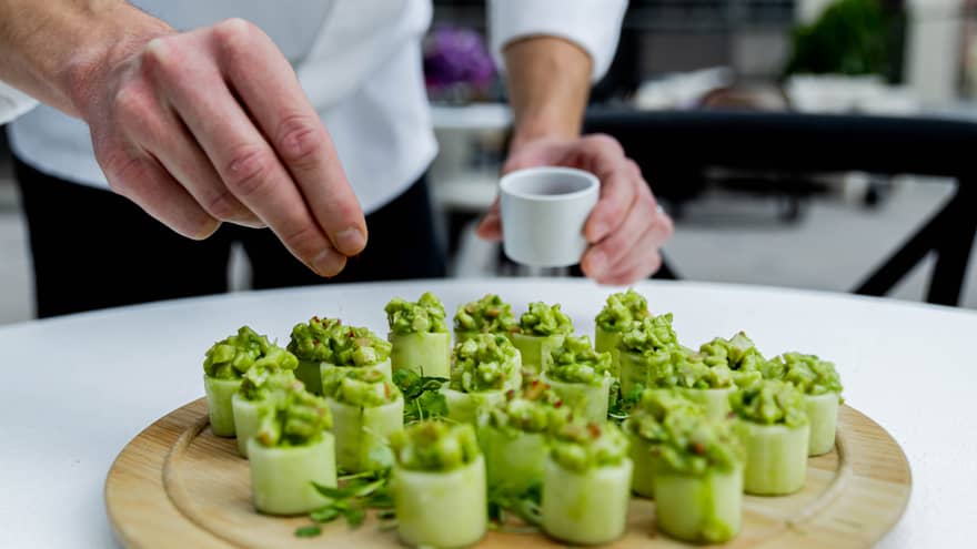 A chef seasoning a green dish made of vegetables on a wood round tray.