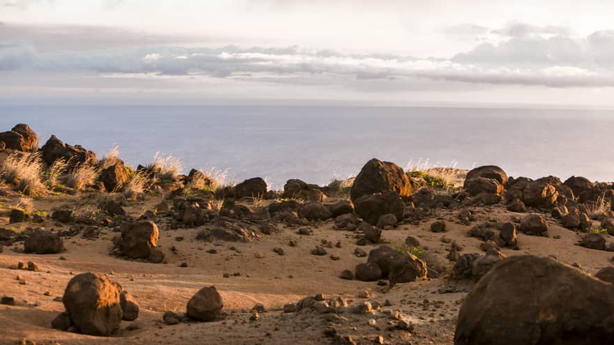 Rocky cliffside at sunset overlooking the ocean, wispy white clouds above