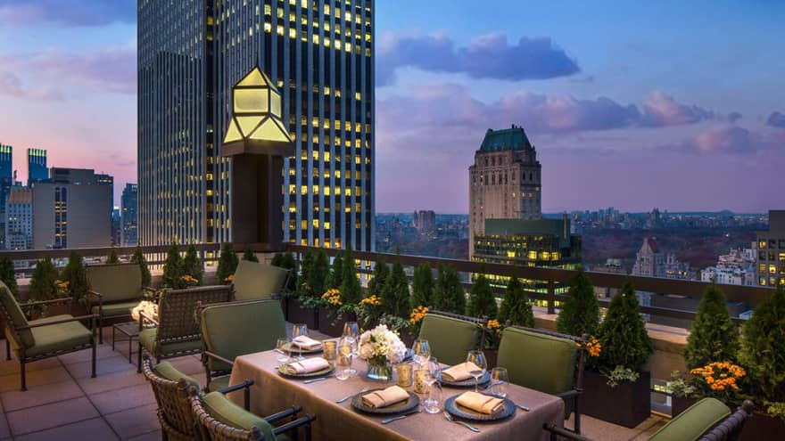 Private patio dining table with plush green cushions on chairs on rooftop terrace, city views at dusk