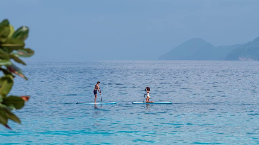 Man and woman paddle board on the open ocean, mountains visible through the fog