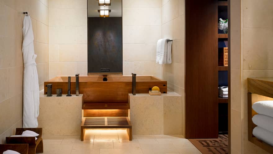 White bathrobe hanging in Master bedroom bathroom with wood Japanese soaking tub, marble ledge, tile walls