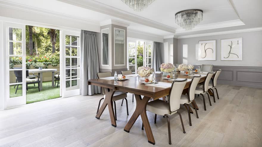 A meeting room with long wooden table, beige chairs and open patio doors.