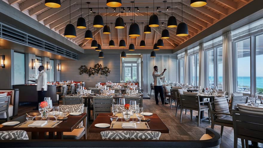 Servers set tables in spacious Dune dining room with soaring ceilings, lights hanging from beams