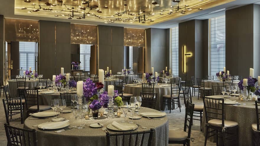 Round banquet dining tables with purple flower arrangements under modern ceiling, lights 