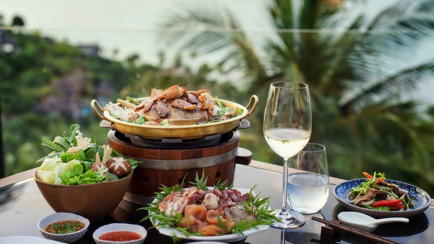 Four plates of food, glass of water and white wine, tropical scenery in background