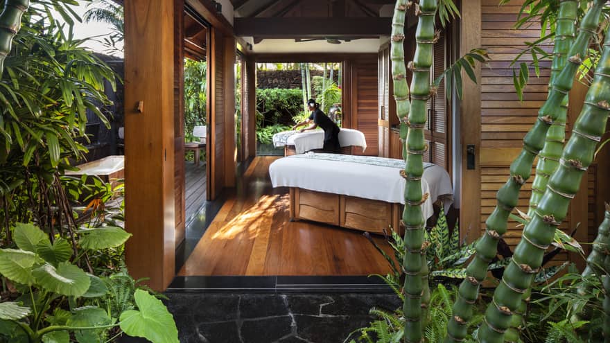 Spa staff spreads sheet on couples massage beds on open-air pavilion 