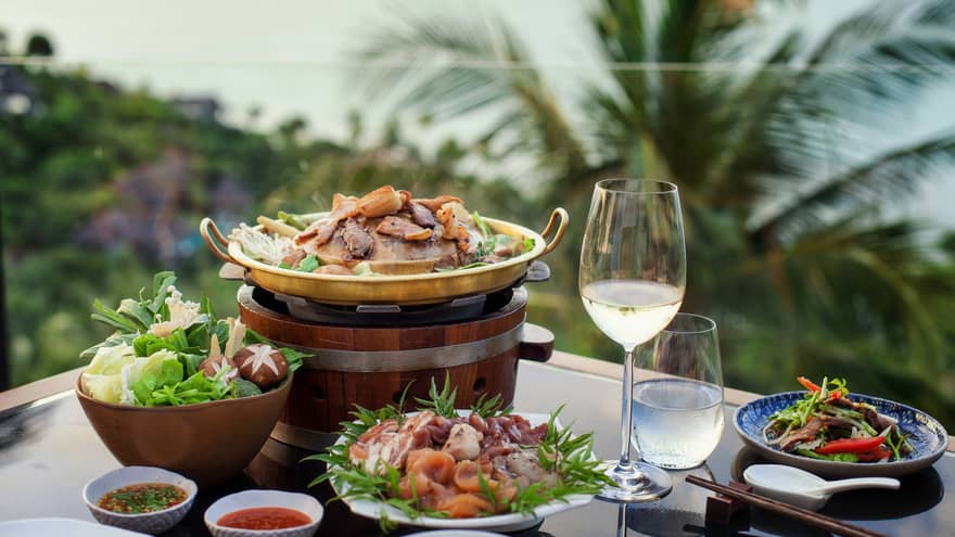 Four plates of food, glass of water and white wine, tropical scenery in background
