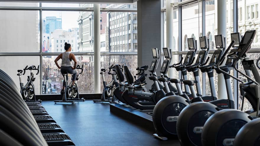 Equinox Fitness Centre, woman on exercise bike by floor-to-ceiling windows, row of cardio machines