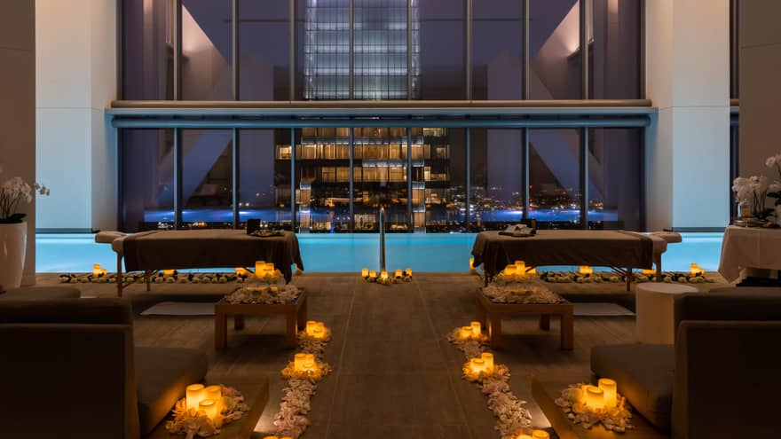 A spa room with candles on the floor and a large window looking out at a city at night.