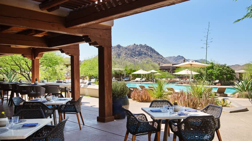 Outdoor patio with table and chairs, view of the pool, and mountains in the background.