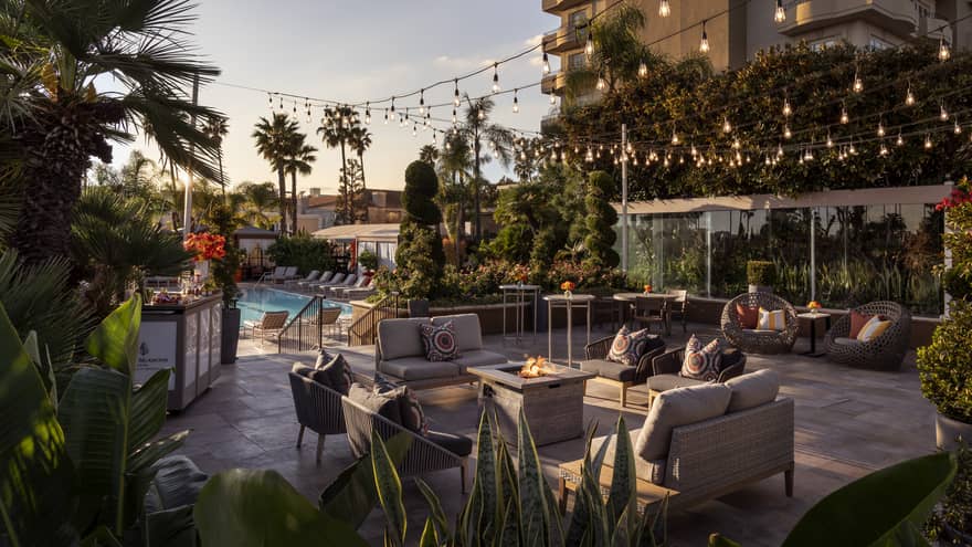 An outdoor seating area with fairy lights next to a pool and palm trees.