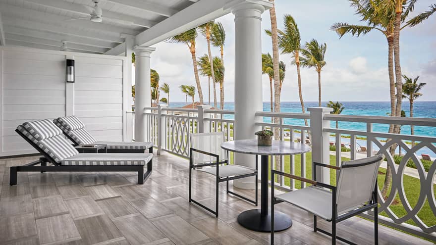 Striped lounge chairs, glass patio table on white balcony with pillars, ocean views