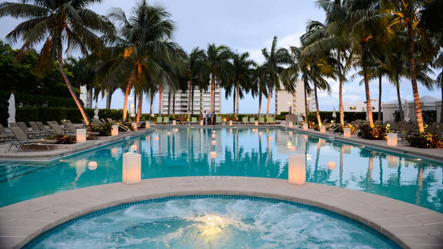 White lanterns glow along outdoor pool lined with palm trees