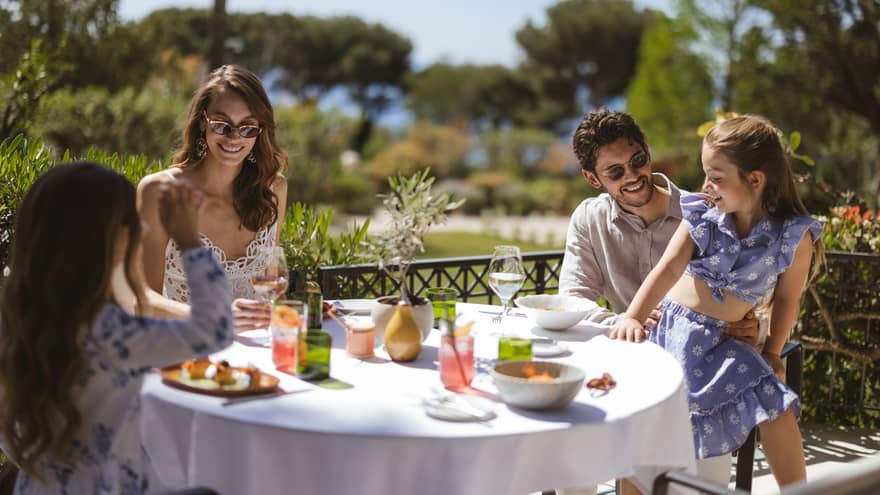 Family of four having a meal at a terrace table on a sunny day