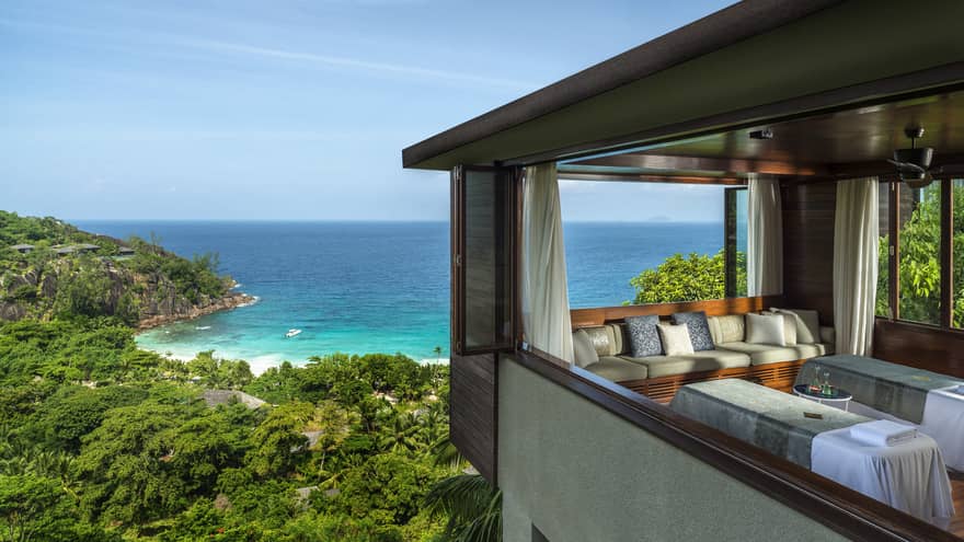 Two side-by-side massage tables in spa room high above trees, ocean