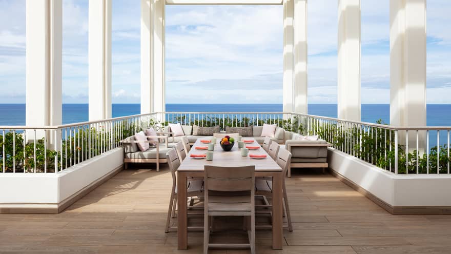Ocean-view terrace of a luxury resort suite, featuring a large dining table and lounge furniture under a white pergola