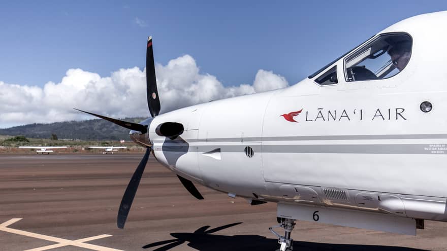 Passenger plane marked Lana'i Air (nose, front propeller and view of pilot in cockpit window), mountains in background