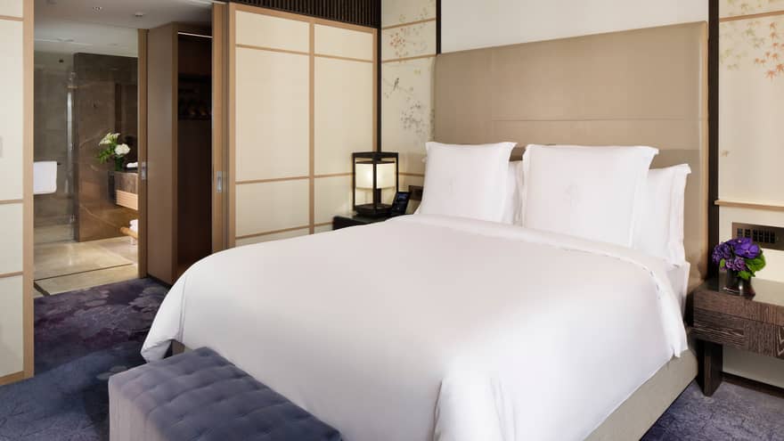 Elegant bedroom with a king-size bed, soft accent lighting, and sliding doors leading to a spacious bathroom at Four Seasons